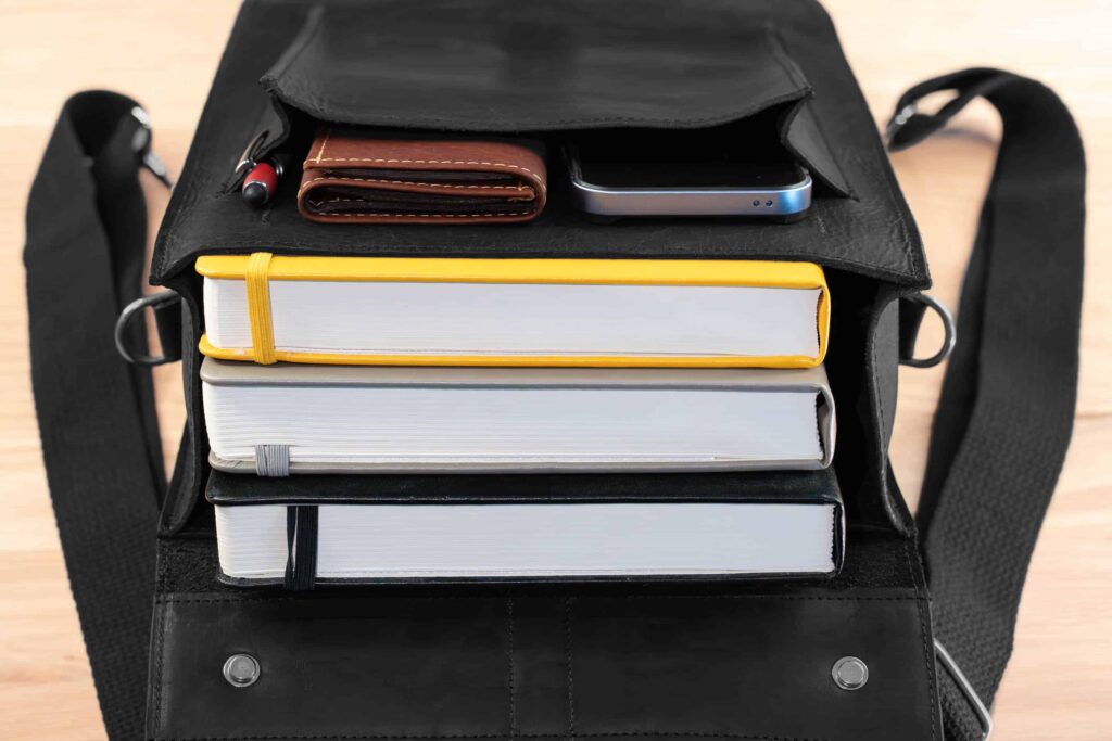 Inside Of Leather Backpack Filled With 3 Thick Books In The Main Compartment, And An Iphone, Wallet, And Pen In The Secured Front Pocket. Inside Of Leather Backpack Filled With 3 Thick Books In The Main Compartment, And An Iphone, Wallet, And Pen In The Secured Front Pocket.