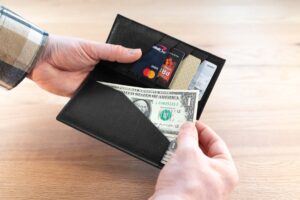 Person Taking A Dollar Bill Out Of The Bill Slot On The Black Leather Checkbook Wallet.